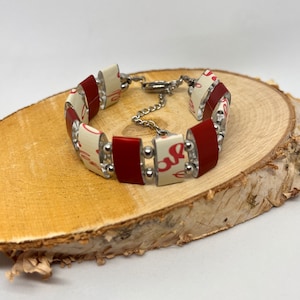 Könnte beinhalten: Ein rot-weißes Armband aus recycelten Materialien. Das Armband besteht aus kleinen Quadraten mit einem silbernen Kettenverschluss.
