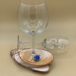 May include: Two clear glass wine glasses on a set of wooden coasters. A blue decorative accent is on the coaster under the glass.