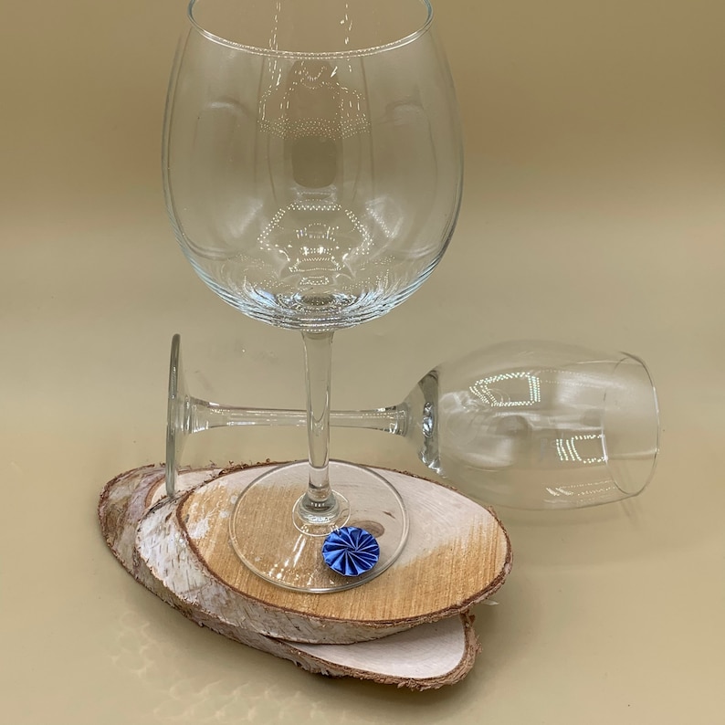 May include: Two clear glass wine glasses on a set of wooden coasters. A blue decorative accent is on the coaster under the glass.