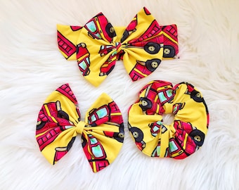 May include: Three yellow and red hair bows with a fire truck print. The bows are in different sizes and styles, including a headband, a large bow, and a scrunchie.