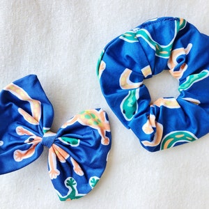 May include: Two blue hair scrunchies with a pattern of orange and green lizards. One scrunchie is tied in a bow.