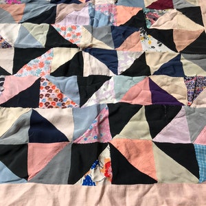 May include: A patchwork quilt made of various fabrics in shades of pink, blue, black, and white. The quilt is made up of triangular pieces sewn together to create a geometric pattern.