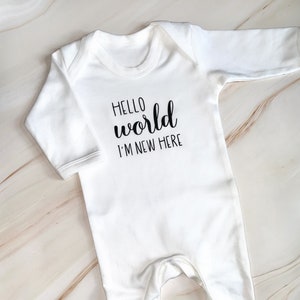 May include: White baby grow with long sleeves and the text "Hello world I'm new here" printed in black.