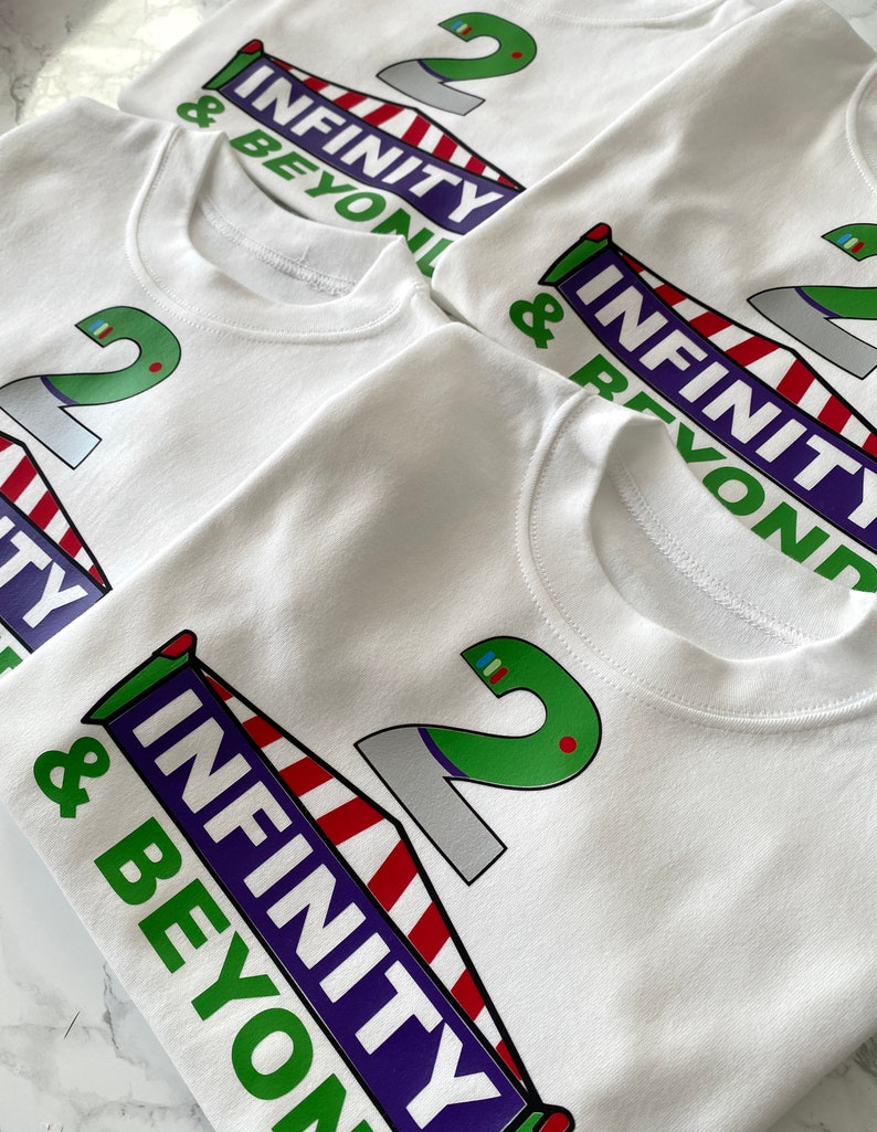 May include: Four white t-shirts with a green number 2 and the words "Infinity & Beyond" printed on them. The shirts are stacked on top of each other.