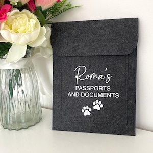 May include: Grey felt passport holder with the name "Roma's" and the text "Passports and Documents" in white lettering. Two white paw prints are below the text.