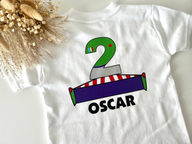 May include: White t-shirt with a green number 2, a red and white striped base, a purple rectangle, and the name "OSCAR" printed on the back.