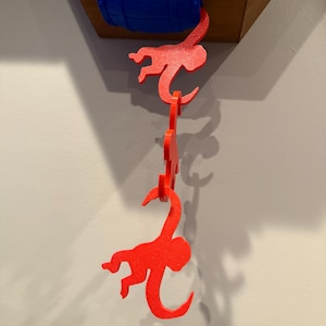 May include: A whimsical wall decoration featuring a blue barrel and three red monkey cutouts hanging below. The monkeys are connected, creating a playful cascade effect. The barrel is mounted on a wooden surface.