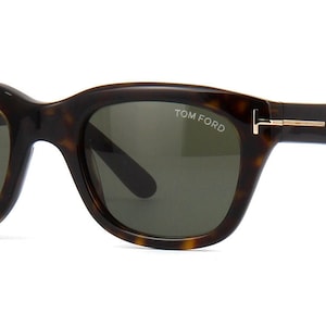 May include: Tortoiseshell sunglasses with dark green lenses and gold accents. The sunglasses have the text "TOM FORD" printed on the right lens.