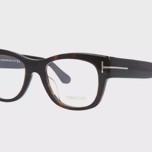 May include: Dark brown and tortoise shell eyeglasses with clear lenses. The frames have a thick, rectangular shape with a silver accent on the temples. The brand name "TOM FORD" is visible on the lens.