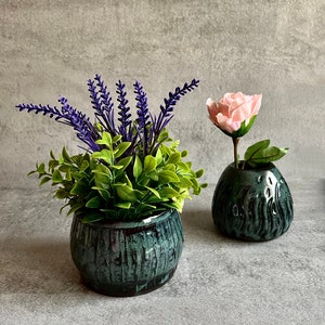 Könnte beinhalten: Zwei Keramik-Blumentöpfe mit grüner Glasur. Ein Topf enthält einen Strauß lilafarbener Lavendel und grünes Laub. Der andere Topf enthält eine einzelne rosa Rose.