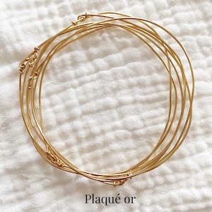 Puede incluir: Un conjunto de pulseras de alambre chapadas en oro. Las pulseras están apiladas una encima de la otra y están hechas de alambre fino. El texto "Plaqué or" es visible en la parte inferior de la imagen.