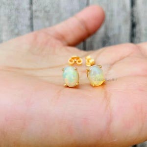May include: A pair of gold oval opal stud earrings. The earrings are set in a simple gold setting and feature a white opal gemstone.