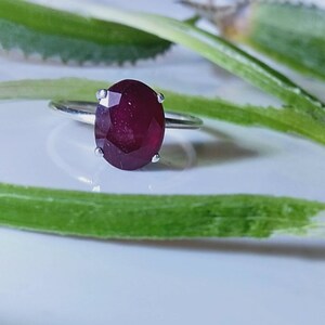 May include: A silver ring with a large, oval-shaped ruby gemstone. The ruby is a deep red color and has a faceted cut.