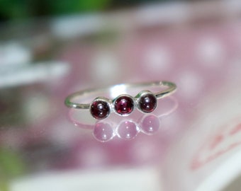 Può includere: Un anello d'argento con tre pietre rotonde di colore rosso scuro.