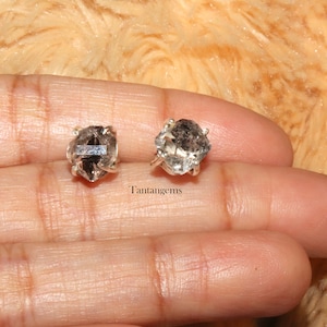 Peut inclure: Une paire de boucles d'oreilles en argent avec des pierres de quartz clair et fumé. Les pierres sont serties dans un sertissage à bélière et ont un aspect brut et naturel. Les boucles d'oreilles sont une façon unique et élégante d'ajouter une touche d'éclat à n'importe quelle tenue.