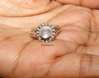 May include: A silver ring with a round moonstone set in a flower-shaped design. The ring is on a hand.