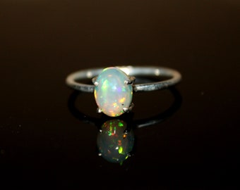 May include: A silver ring with a white opal gemstone. The opal has a rainbow sheen.