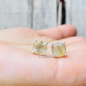 May include: A pair of silver earrings with square-shaped gold rutilated quartz gemstones. The earrings are set in a simple, modern style.