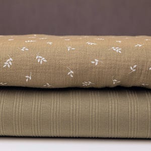 Könnte beinhalten: Zwei Stoffstücke, eines mit hellbraunem Hintergrund und einem weißen Blatt-Muster, das andere einfarbig hellbraun mit gerippter Textur.