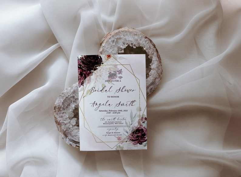 May include: A white bridal shower invitation with a gold geometric frame and floral design. The invitation reads "Join us for a Bridal Shower to honour Angela Smith" and includes the date, time, and location of the event.