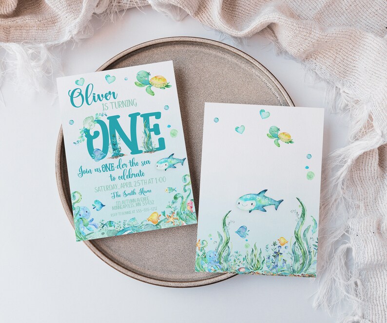 Peut inclure: Une carte d'invitation bleue et verte avec une illustration aquarelle d'une tortue de mer, d'un requin et d'autres cr&eacute;atures marines. Le texte sur la carte indique "Oliver a un an. Rejoignez-nous sous la mer pour c&eacute;l&eacute;brer Samedi 25 avril &agrave; 13h00 Chez les Smith".