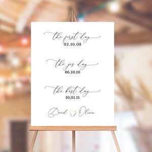 May include: White sign with black calligraphy text on an easel. The text reads "the first day 02.10.08", "the yes day 06.10.10", and "the best day 10.01.11". The sign is signed "David & Olivia" with a heart symbol.
