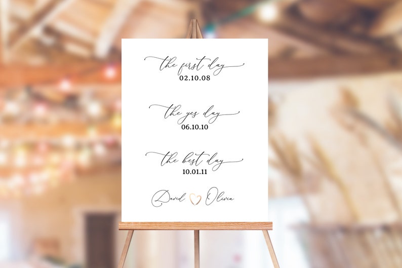 May include: White sign with black calligraphy text on an easel. The text reads "the first day 02.10.08", "the yes day 06.10.10", and "the best day 10.01.11". The sign is signed "David & Olivia" with a heart symbol.