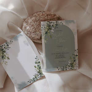 May include: Two wedding invitations with a watercolor floral design. The invitations are on a white background with a light blue border. The text on the invitation reads "Bridal Shower" and "Olivia & Luke".