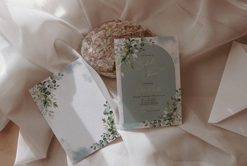 May include: Two wedding invitations with a watercolor floral design. The invitations are on a white background with a light blue border. The text on the invitation reads "Bridal Shower" and "Olivia & Luke".