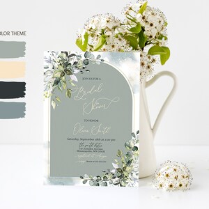 May include: A light blue and white bridal shower invitation with a gold border and a watercolor floral design. The invitation reads "Join us for a Bridal Shower to honor Olive Smith, Saturday, September 18th at 2:00 pm, The Smith Bistro, 111 Autumn Avenue, Minneapolis, MN 55422, RSVP by August 15th".