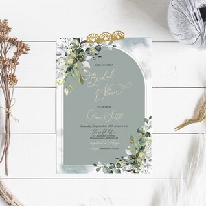 May include: A light blue and white bridal shower invitation with gold accents. The invitation features a watercolor illustration of eucalyptus leaves and a gold arch. The text on the invitation reads "Join us for a Bridal Shower" and "To Honor Olivia Smith".