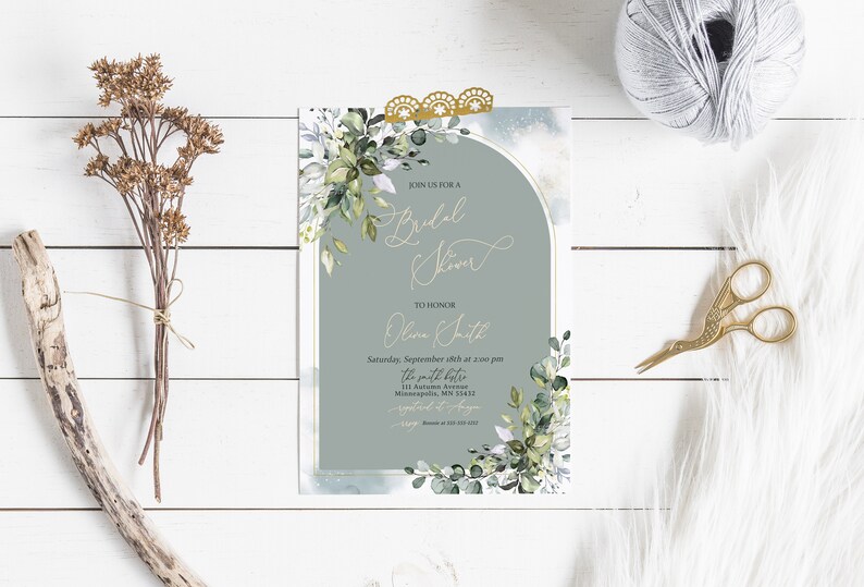 May include: A light blue and white bridal shower invitation with gold accents. The invitation features a watercolor illustration of eucalyptus leaves and a gold arch. The text on the invitation reads "Join us for a Bridal Shower" and "To Honor Olivia Smith".