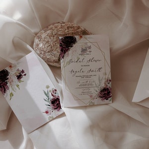 May include: A white card with gold accents and floral designs. The text on the card reads "Join us for a Bridal Shower to honour Angela Smith".