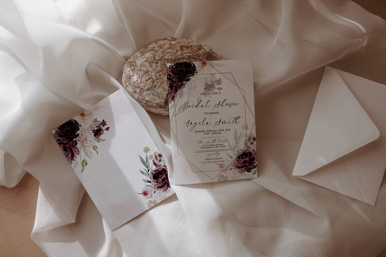 May include: A white card with gold accents and floral designs. The text on the card reads "Join us for a Bridal Shower to honour Angela Smith".