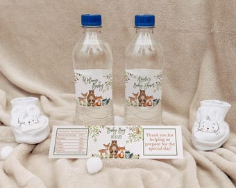 May include: Two clear plastic water bottles with labels featuring woodland animals and the text "Welcome Baby" and "Baby Shower". The bottles are on a light brown surface with two white bunny-shaped baby booties.