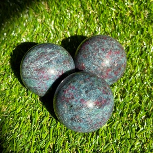 Op de afbeelding: Drie groene en rode edelsteen bollen op een groene kunstgras achtergrond.