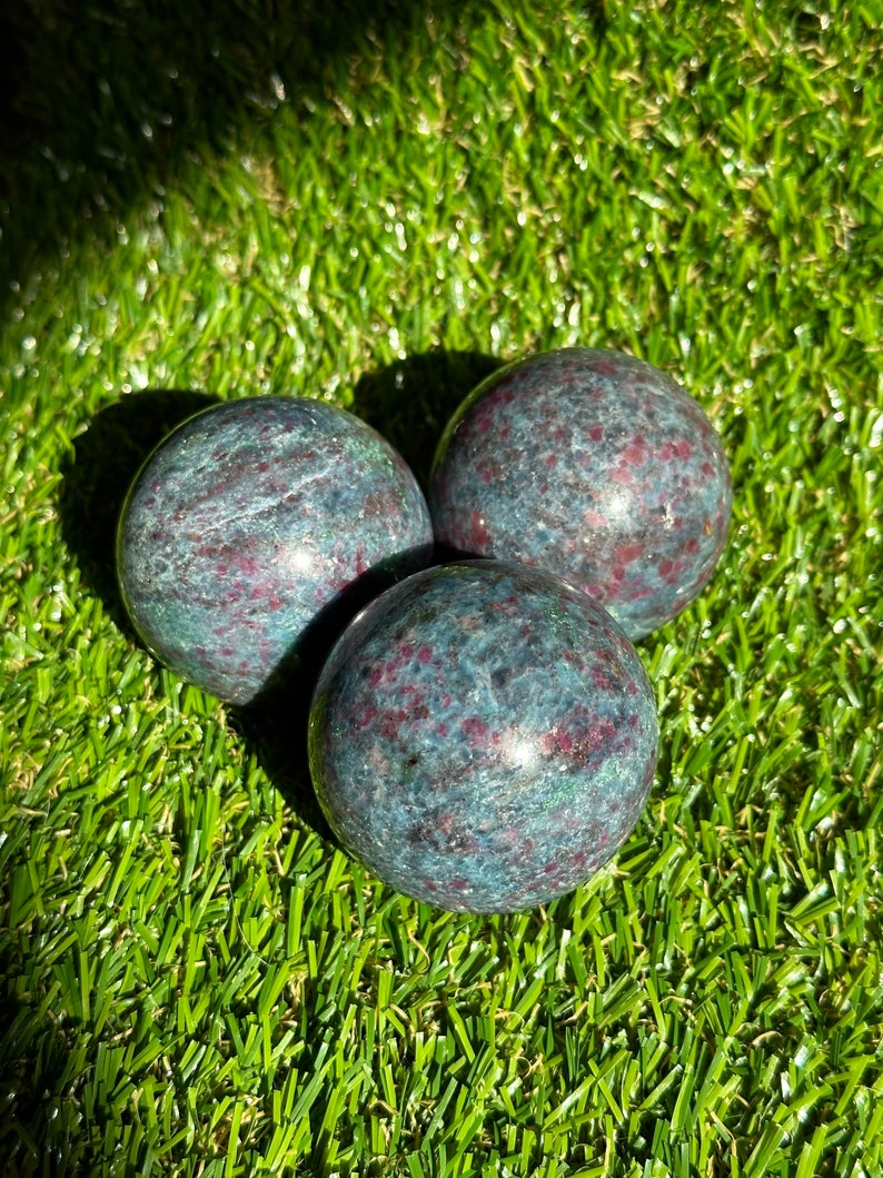 Op de afbeelding: Drie groene en rode edelsteen bollen op een groene kunstgras achtergrond.