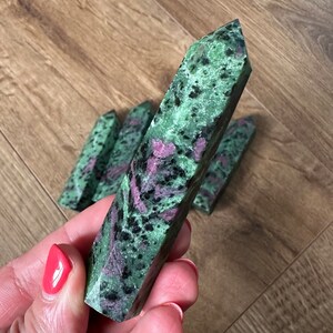 May include: A collection of green, pink and black gemstone points. The points are polished and have a smooth, shiny finish.