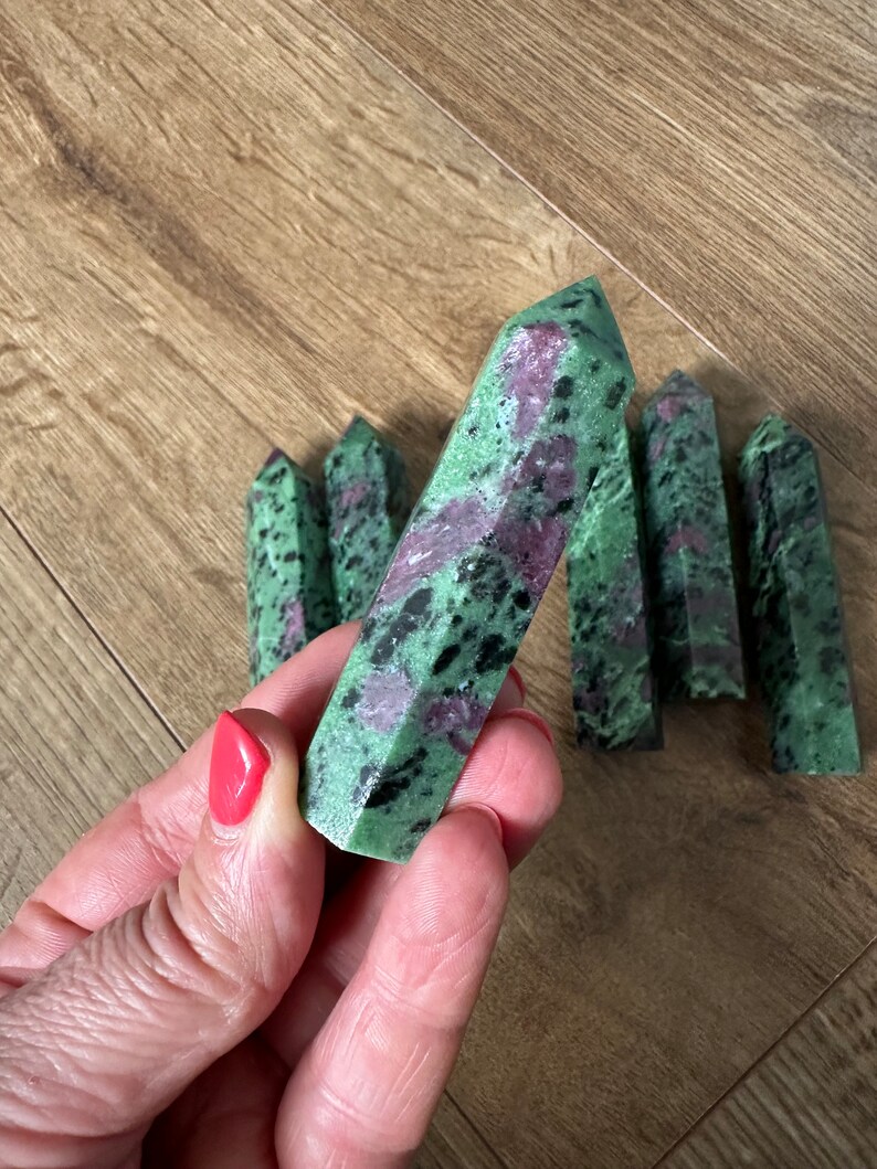 May include: A collection of green, pink and black gemstone points. The points are polished and have a smooth, shiny finish.