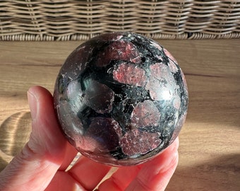 May include: A black and red sphere with a speckled pattern. The sphere is made of polished stone and has a smooth, glossy finish.