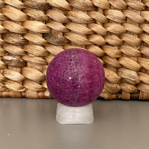 Peut inclure: Une sph&egrave;re violette avec une base blanche. La sph&egrave;re est faite d'un mat&eacute;riau naturel et a une texture rugueuse.