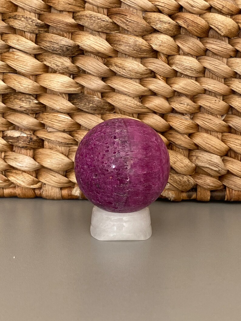 Peut inclure: Une sph&egrave;re violette avec une base blanche. La sph&egrave;re est faite d'un mat&eacute;riau naturel et a une texture rugueuse.