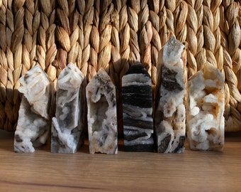 May include: Six agate crystal points in various shades of brown, white, and black. The points are arranged in a row on a wooden surface.