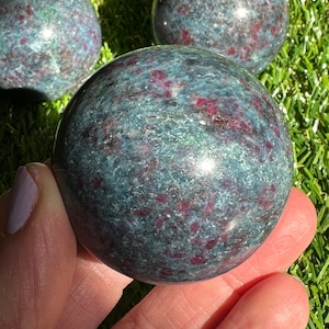 Op de afbeelding: Drie groene en rode edelsteen bollen, &eacute;&eacute;n wordt in een hand gehouden. De bollen zijn gepolijst en hebben een gevlekt uiterlijk.