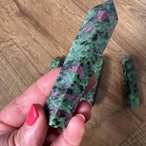 May include: A collection of green and pink zultanite gemstone points. The points are smooth and polished, with a variety of shades of green and pink.