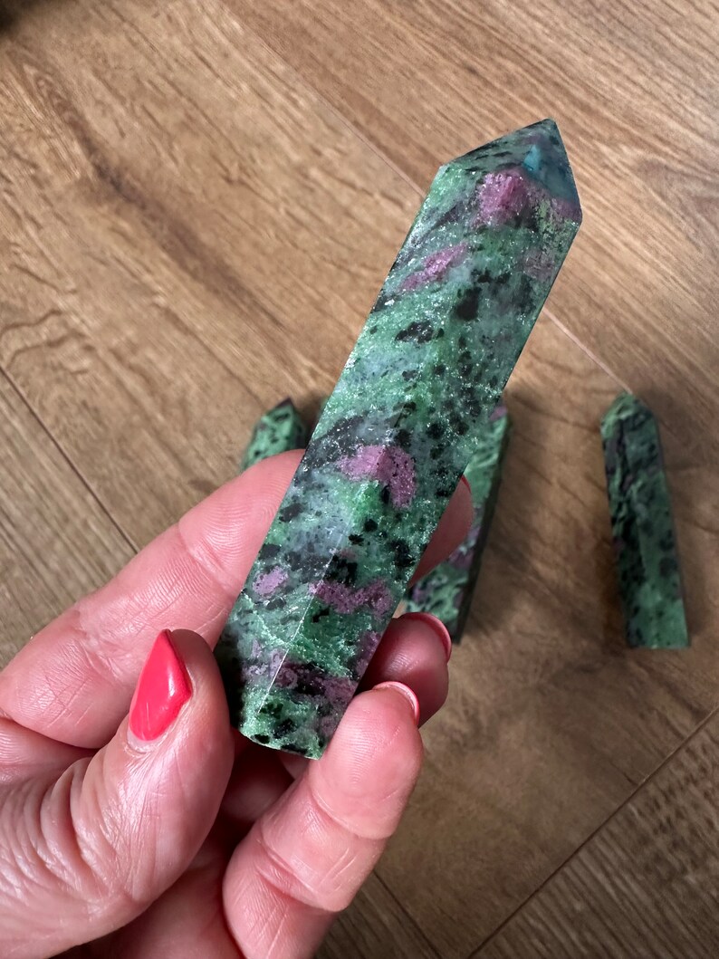 May include: A collection of green and pink zultanite gemstone points. The points are smooth and polished, with a variety of shades of green and pink.