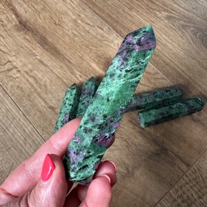May include: A collection of green and pink gemstone points, also known as zoisite, arranged on a wooden surface. The points are smooth and polished, with a variety of shades of green and pink.