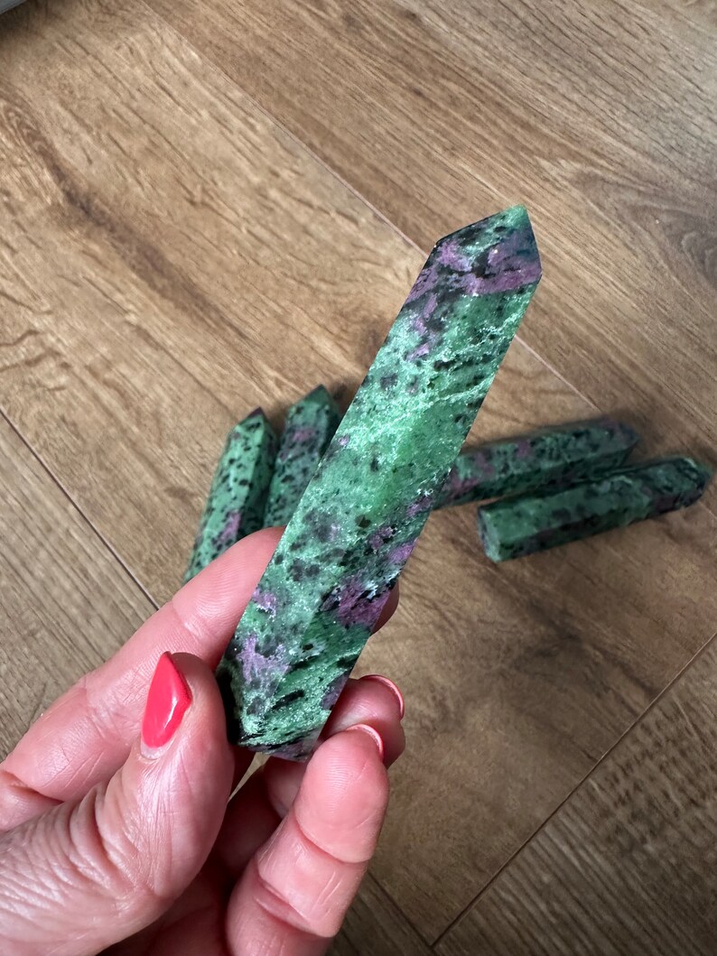 May include: A collection of green and pink gemstone points, also known as zoisite, arranged on a wooden surface. The points are smooth and polished, with a variety of shades of green and pink.