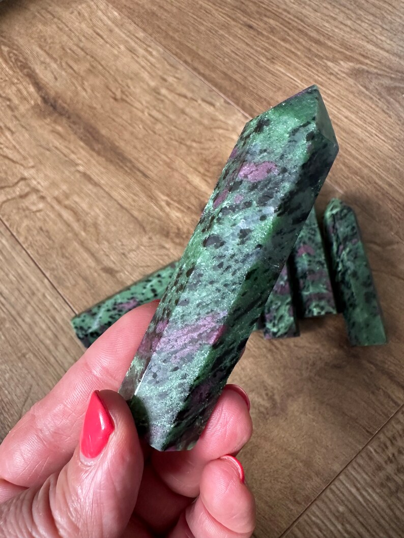 May include: A collection of green and pink zultanite gemstone points. The points are smooth and polished, with a variety of shapes and sizes.
