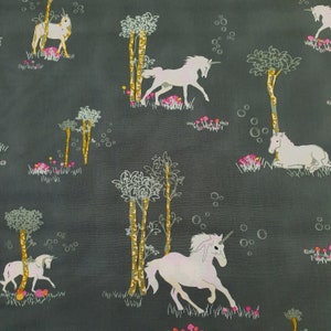 Puede incluir: Tela gris oscuro con un patrón repetido de unicornios blancos, árboles y flores rosas. Los unicornios están en varias poses. Los árboles tienen troncos dorados y follaje blanco. Diseño caprichoso.